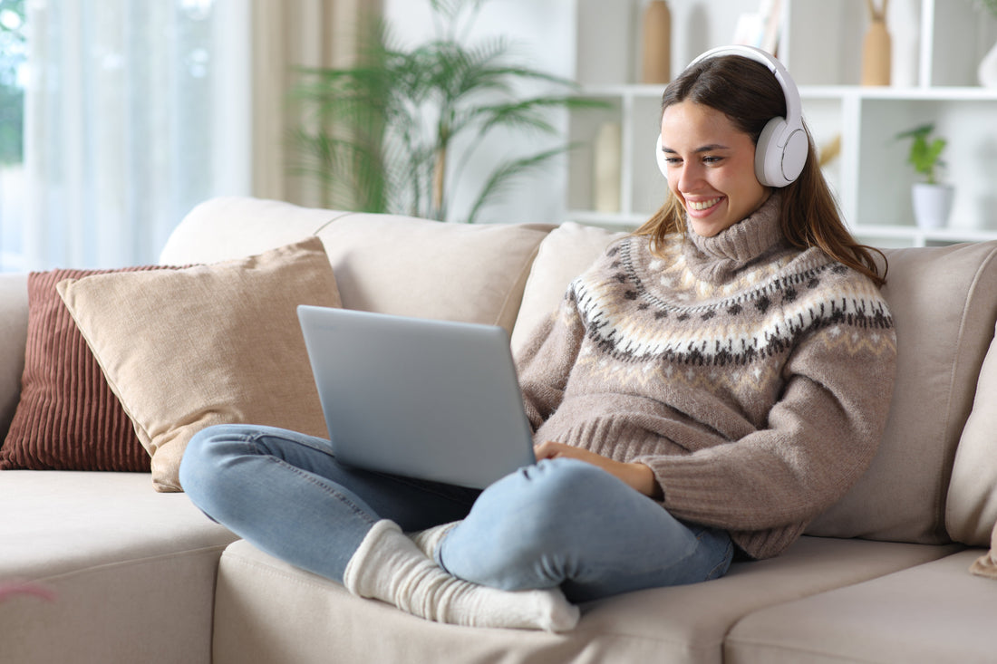 Woman with headphones on, sat on sofa using a laptop.