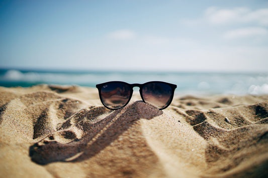 sunglasses laid in the sand on a beach
